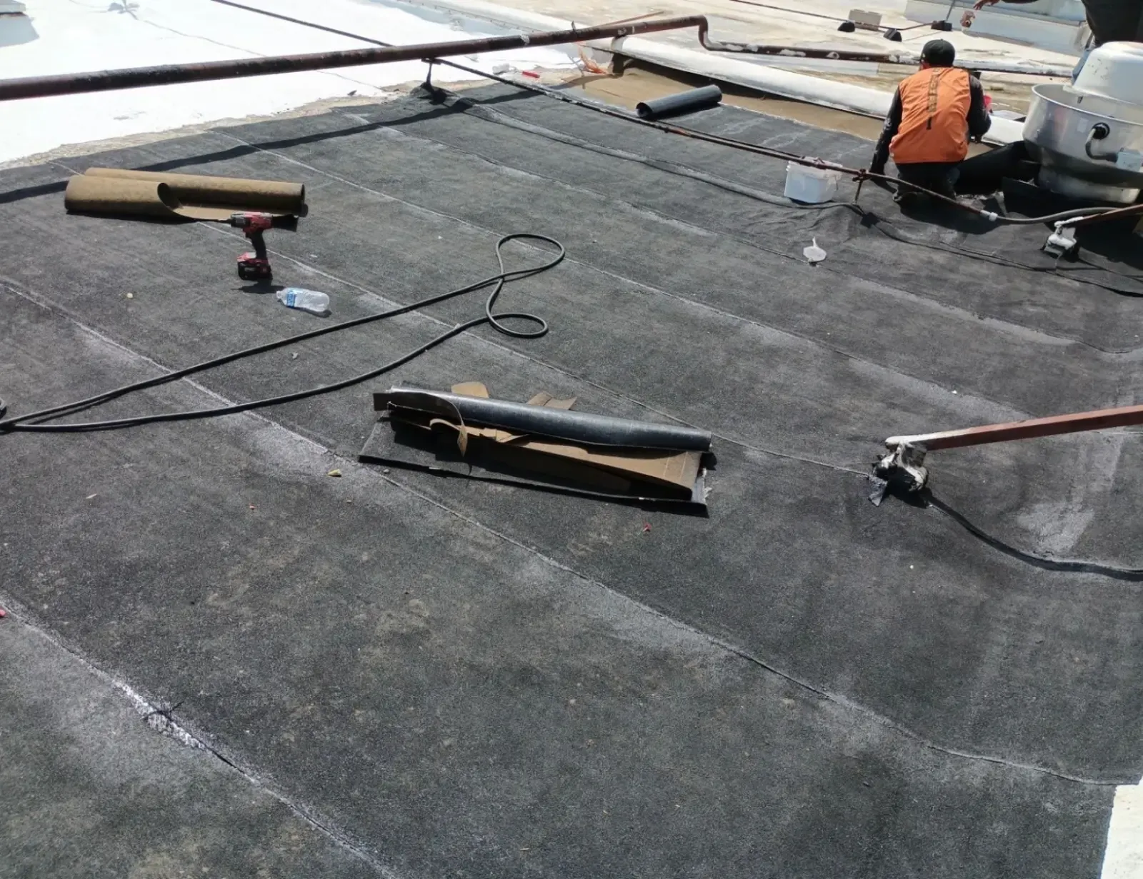 Crew installing new rolled roofing around a rooftop exhaust fan on a commercial building