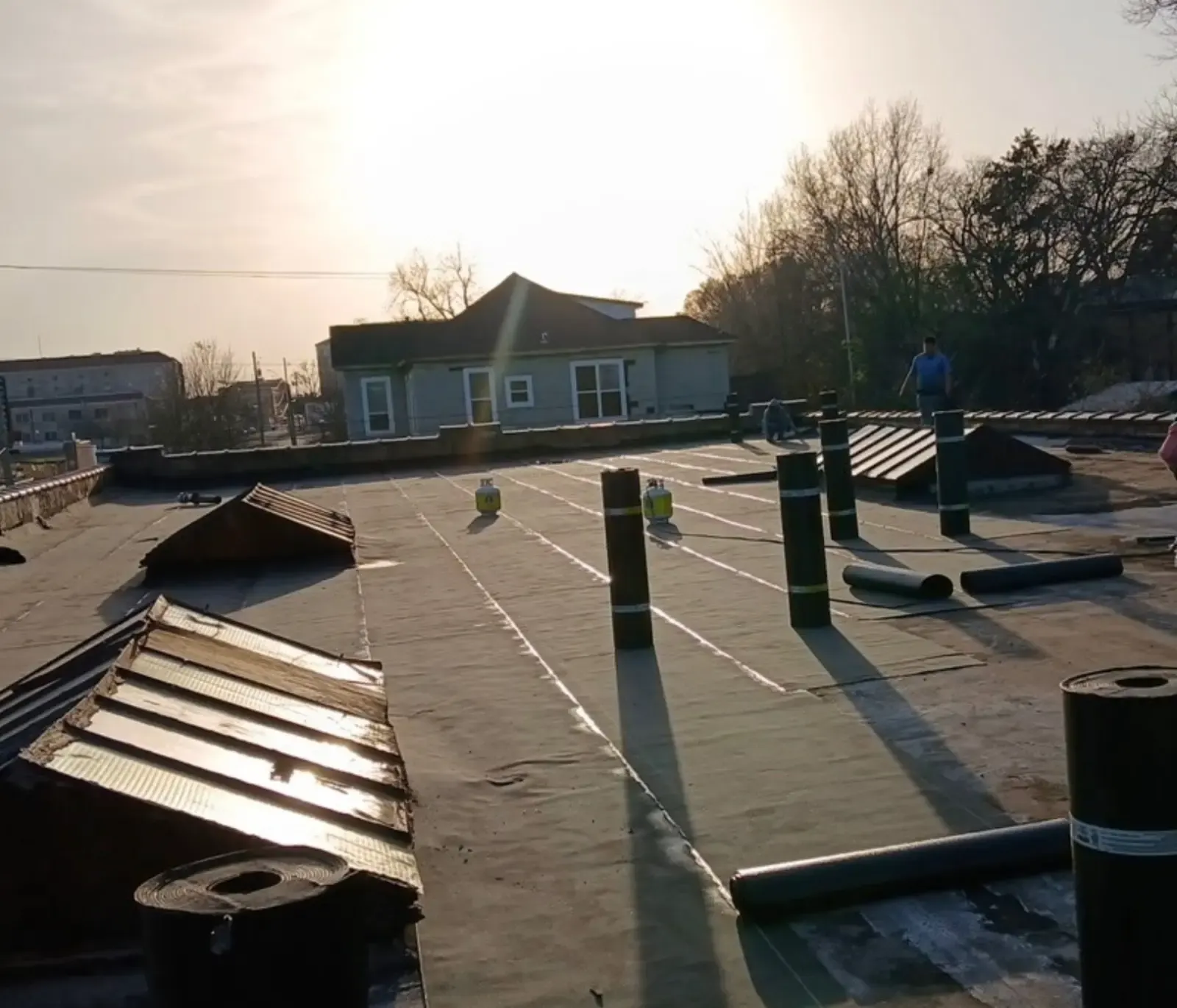 Commercial flat roof partway through, with rolls of roofing laid out at sunset